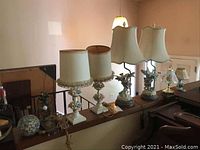 Seven lamps and a separate glass globe lined up on ledge