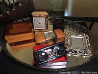 Overview of all lot items on brass framed mirrored tray including clocks, wooden boxes, binoculars, and sculpture.