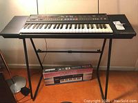 Full view of Yamaha PSR-27 keyboard mounted on black stand with Casio PT-100 keyboard box underneath.