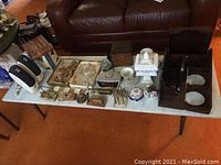 Wide view of table with various items including marble chess set trays, wooden boxes, ceramic trays, two wooden shelves, speakers, and a clip-on lamp.