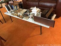 Side view of the rectangular coffee table showing the white marble top, metal legs, and items placed on the table including wooden closet organiser and decorative pieces.