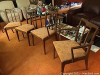 Photo showing all four Mid-Century Modern wooden dining chairs arranged in a row on carpet. Two captain chairs with armrests and two mate chairs without armrests visible with patterned upholstery.