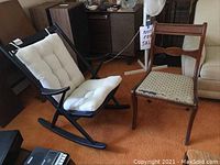 View showing both the black rocking chair with white removable cushions and the vintage wooden chair with patterned upholstery displaying wear and scratches.