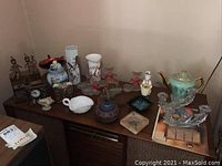 Overview of the lot showing porcelain vases, metal figurines, teapot, clocks, candle holders, and bowls on a wooden cabinet