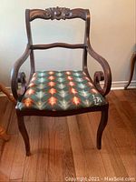 Front view of mahogany-finished wood armchair with carved backrest and needlepoint seat