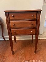 Front view of wooden sewing cabinet showing three drawers with round knobs and four legs.