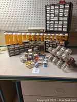 Overall view of various organizers, jars, and pill bottles containing screws, bolts, nuts, and small hardware items on workbench.