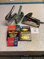 Photo showing three staplers (two manual and one electric) and four boxes of Arrow staples on a table.