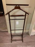 Frontal view of the wooden valet stand showing the garment hanger, trouser bar, and accessory rack.
