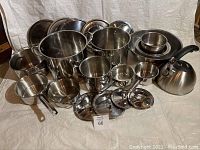 Front view of the stainless steel pots, bowls, and whistle kettle arranged together on white backdrop showing the full set including lids and handles.