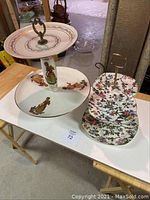 Two multi-tiered serving platters on a white table, one with traditional figure illustrations and one with floral pattern.