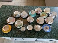 Photo showing the entire set of 13 assorted teacups and saucers arranged with the sugar bowl, small sugar bowl, and creamer on a counter.