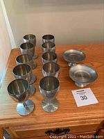 10 pewter wine goblets arranged in rows with 2 pewter candy dishes on a wooden surface