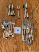 Photo of 47 pieces of assorted stainless steel cutlery arranged on wooden surface: forks, knives, spoons, butter spreader, with auction tag in center
