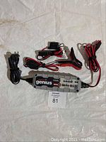 Photo of Norco Genius G3500 battery charger with connected cables, clamps, and plug attachments laid flat on a surface.