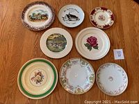 Eight assorted decorative plates arranged on a wooden table showing various designs and sizes.