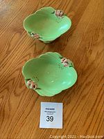 Two green leaf-shaped candy dishes with pink floral accents photographed on a wooden table from above showing shape and colors.