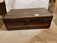 Front view of antique wooden steamer trunk showing wood slats, metal bands and central locking latch.
