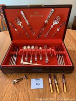 Full open velvet-lined wood box showing cutlery pieces arranged inside and bonus yellow handled butter spreaders outside