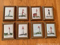 Group photo of all 8 framed cross stitch lighthouse artworks arranged in two rows, showing details of each lighthouse.