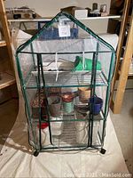 Full view of 3-tier mini greenhouse with clear plastic cover and pots inside