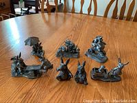 Seven pewter rabbit figurines arranged on wooden table showing all figures.