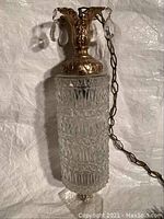 Front view of swag lamp showing metal top with leaf motifs, teardrop glass pendants, and textured cut glass cylindrical body.