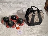 Four black Taylor Lignoid lawn bowls on knitted cloths with orange measuring device and patterned carry bag