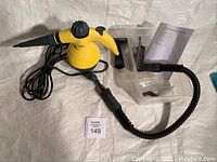 Hotshot steam cleaner with flexible hose attached, power cord coiled nearby, white plastic accessory holder, black brush attachment, and manual on a white backdrop.