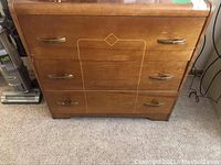 Front view of wooden dresser showing three drawers with metal handles and geometric inlay.