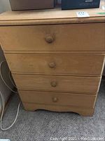 Front view of wooden 4-drawer dresser showing knob handles and surface wear.