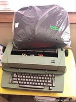 IBM electric typewriter with plastic cover on platen and keyboard visible