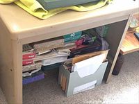 Photo of the metal desk from the front showing underside storage space with loose papers and files (contents not included).