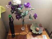 Wooden figurine, glass vase with artificial flowers, leaf-shaped bowl with egg on wooden table.