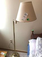 Full view of the floor lamp showing beige lampshade, metal pole, and weighted base.