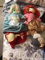 Top view of the two vintage cloth dolls laid on a quilted surface, showing their fabric clothing and yarn hair.