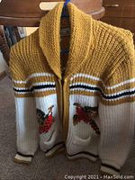 Full view of vintage chunky knit wool sweater hanging on a blue hanger showing shawl collar and bird design on front pockets.