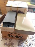 Rollei P 350 autofocus slide projector in cardboard box with slide boxes on top.
