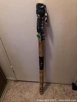 Full length photo of the wooden rain stick showing the wrapped fabric decoration at the top and painted section on the body.