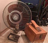 Front angled view of the vintage MasterCraft table top fan with wooden blades and cage, alongside wooden shoe shine box with brush on top.