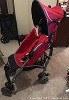 Side view of red collapsible stroller showing seat, wheels, shade canopy, and lower basket in living room setting.