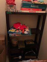 Front view of black plastic four-shelf unit, partially filled with various household items (not included in sale).