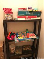 Full view of black shelving unit containing boxed board games and smaller toys such as skipping ropes, Polly Pockets, Beanie Babies, Dr. Seuss game.