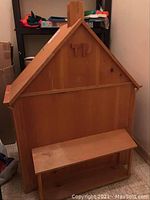Front view of the wooden doll house showing the house shape and wood finish, with scratches visible.
