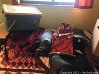 Camping gear set including cooler, backpack, sleeping bag, arranged on bed