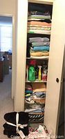 View of closet shelving with folded blankets, throws, sheets, comforters, and some cleaning supplies on the middle shelf