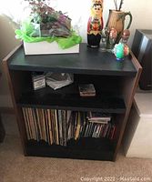 Front view of shelving unit showing two shelves containing papers and vinyl records, topped with decorative items.