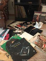 Overview of lot showing multiple LP covers, a vinyl single, cassette tapes and a record shelf in background