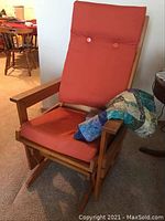 Front angled view of the glider chair showing orange cushion and quilt draped on arm