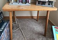 Full view of wooden table on carpeted floor. The table has a rectangular top with wood grain visible and four round legs.